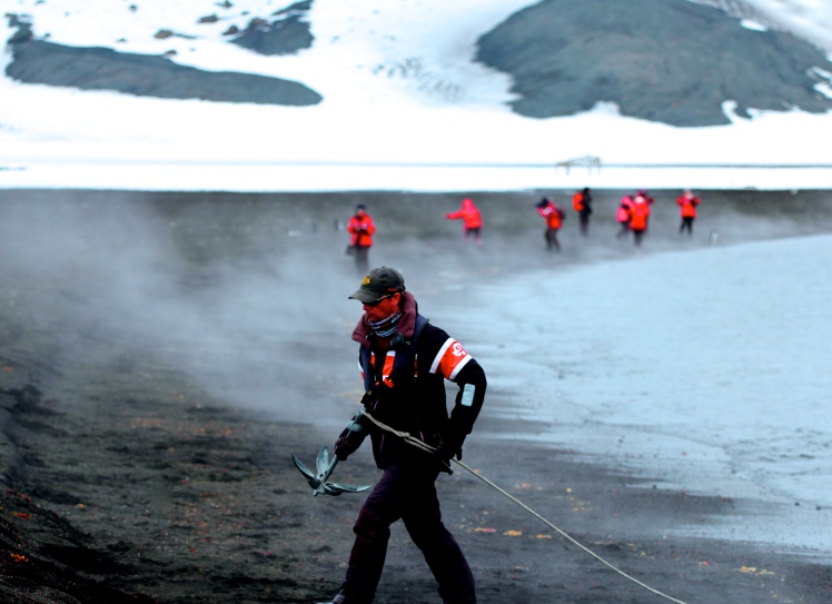 Geology Bob dragging a zodiac onto a volcanic beach, shrouded in geothermic mist 